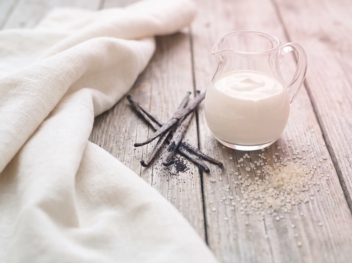 Split vanilla pods, a small glass pitcher of cream and cane sugar on worn wooden boards
